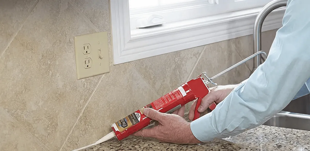 Handyman applying caulk along a kitchen backsplash and countertop seam in Lowell, MA